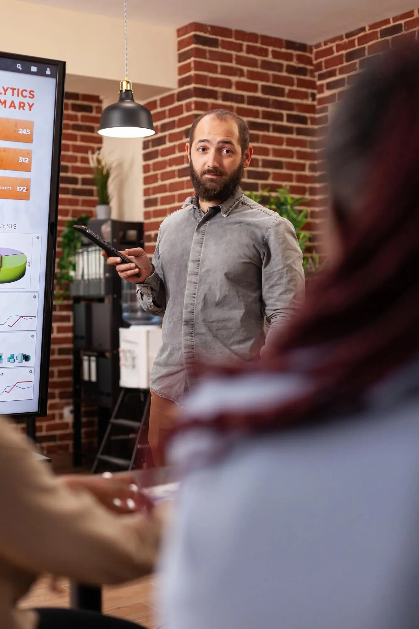 Hombre emprendedor señalando un monitor y explicando estadísticas de gestión al equipo de negocios que trabaja en una presentación de la empresa en la oficina de una startup. Profesionales de negocios diversos planificando una presentación empresarial.